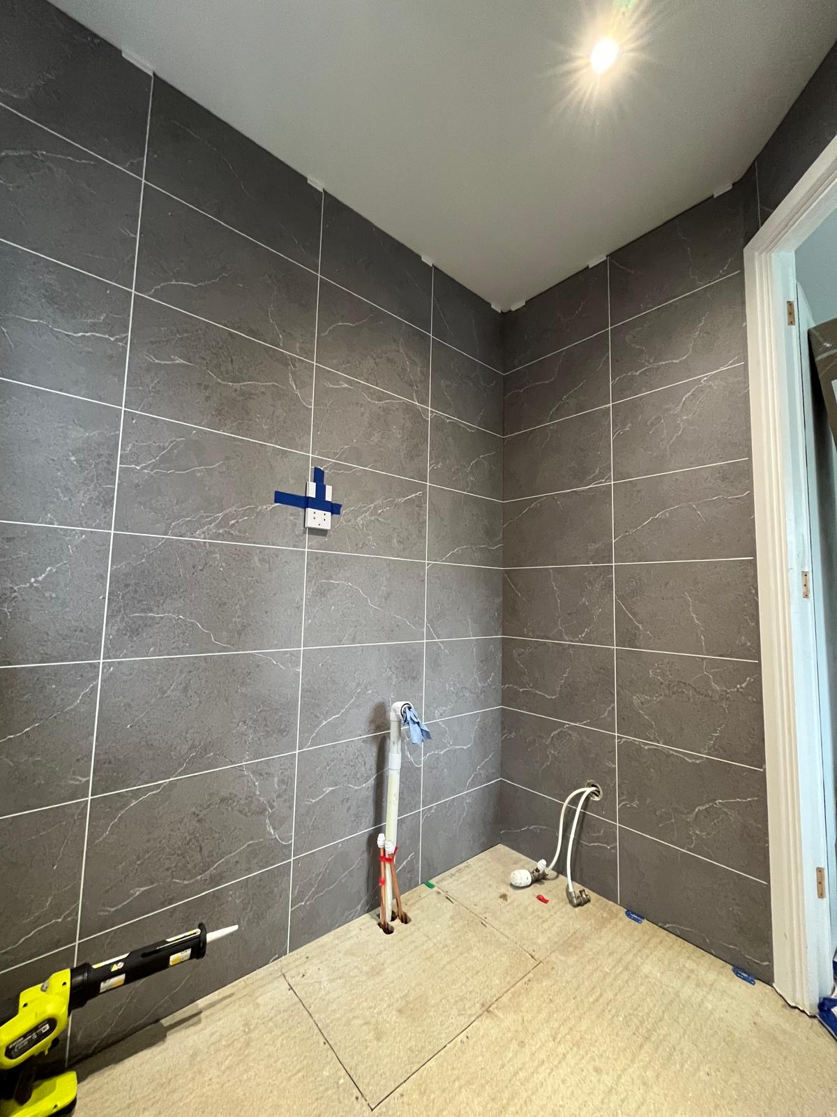 Tiled corner mid-installation with exposed basin pipework and no furniture fitted