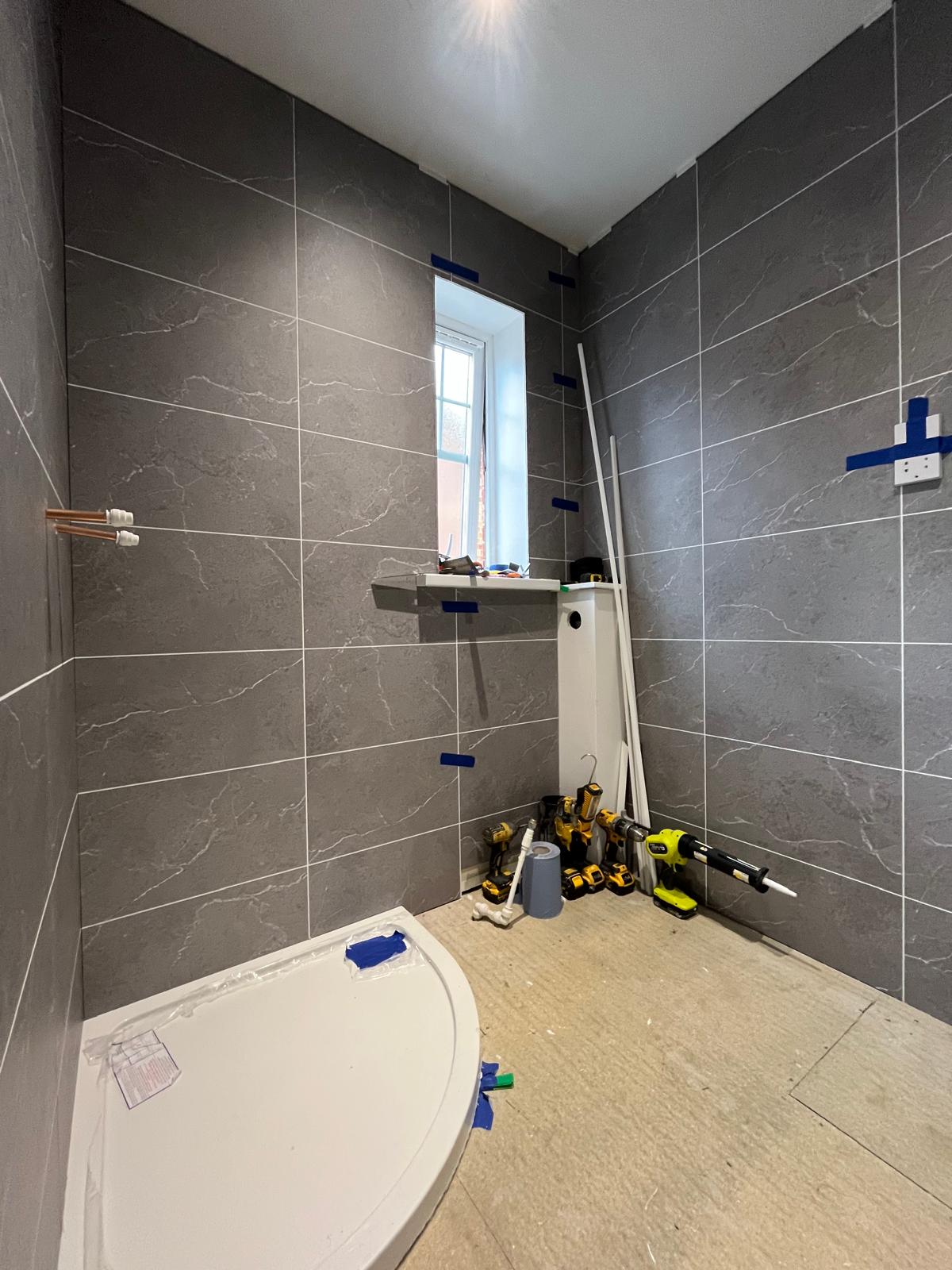 Shower room mid-installation with tiled walls, bare shower tray and exposed pipework