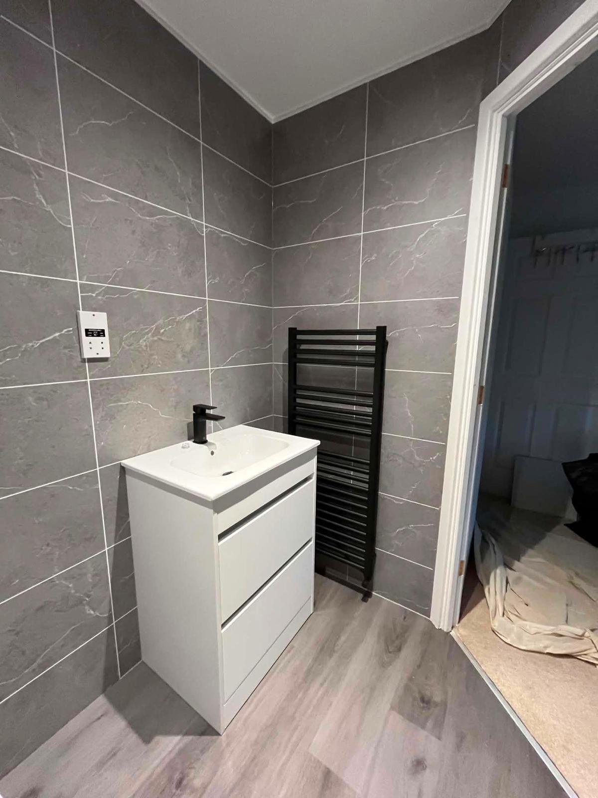 Finished corner with white two-drawer vanity unit, black tap and black ladder towel radiator